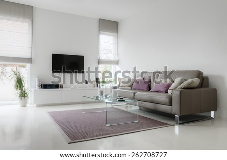White living room with taupe leather sofa and glass table on carpet