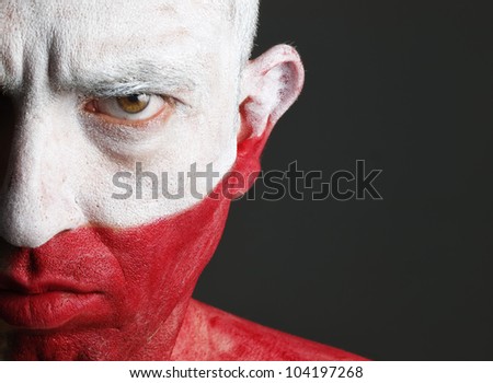 Man with his face painted with the flag of Poland.  The man is serious and photographic composition leaves only half of the face.