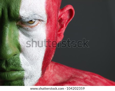 Man with his face painted with the flag of Italy. The man is serious and photographic composition leaves only half of the face.