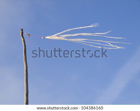 Broken plastic bag used to measure wind direction., Is tied to a pole and flies over a background of blue sky.