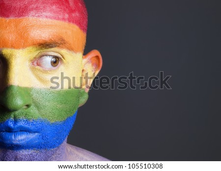 Gay flag painted on the face of a man. Man is looking sideways with restlessness expression.