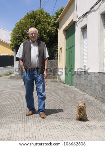 Elderly man walking a dog and looking at camera in an urban setting and on a sunny day