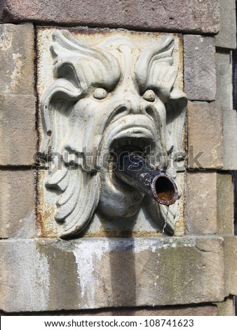 Water fountain shaped gargoyle face. In the mouth has a metal tube that drains the water. The picture was taken in Stockholm.