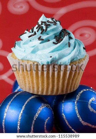 One blue cupcake and two christmas balls on red background