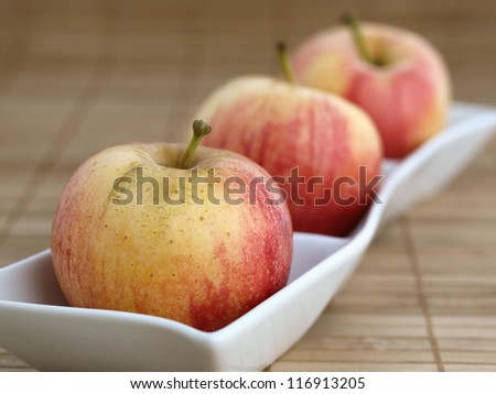 Three apples in a  white bowl