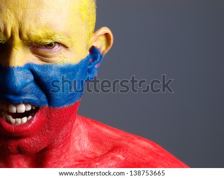 Man face painted with colombian flag. The man is angry and photographic composition leaves only half of the face.