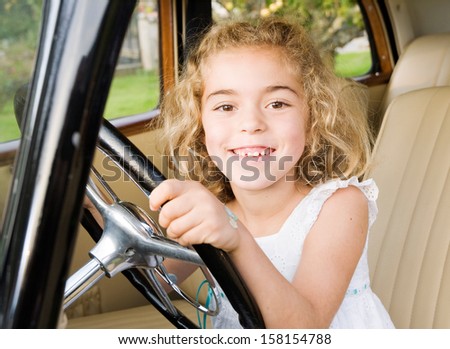 Little girl sitting in an old car and looking at camera with a big smile.