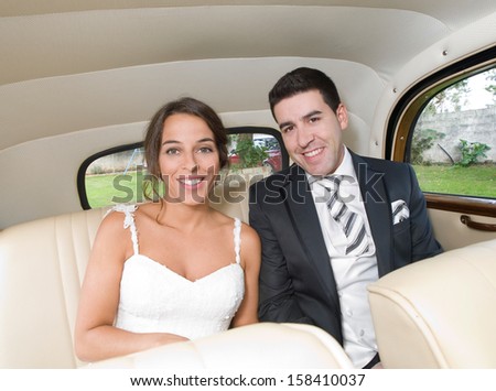 The bride and groom are sitting inside the retro car. They are looking at camera and smiling.