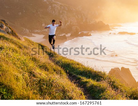 Man practicing trail running and leaping in a path in the coast in a sunny day