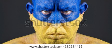 Man with his face painted with the flag of Ukraine.  The man is serious