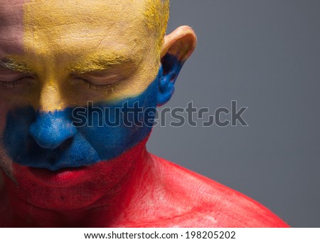 Man and his face painted with the flag of Colombia. The man has his eyes closed and photographic composition leaves only half of the face.