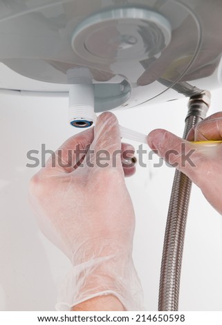 Hands repairing the plumbing pipes of an electric boiler.