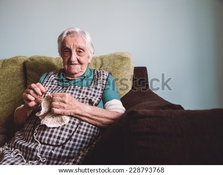 Elderly woman sewing at home. Old lady is happy.