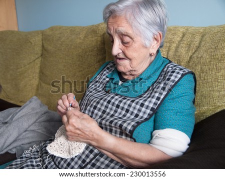 Elderly woman sewing in her home. Elderly woman is sitting on a sofa