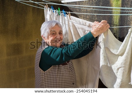 Elderly woman hanging out the washing on the terrace of her house. Woman is smiling.