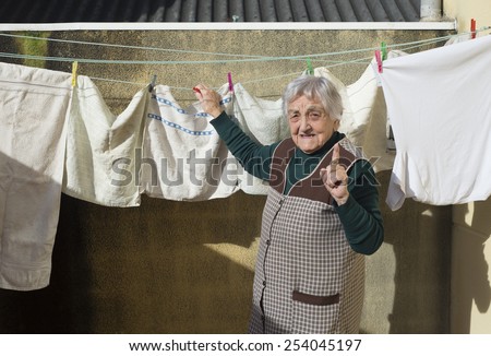 Elderly woman hanging out the washing on the terrace of his house. Woman is looking at camera.