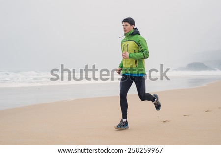 Young man running in the beach in a rainy day. Man is running on the sand.