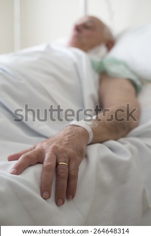 Mature man lying in a hospital bed recovering from surgery.