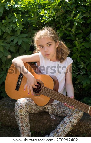 Seven years old girl playing a spanish guitar outdoors