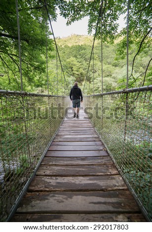 Man crossing a suspension bridge in the forest in the natural park \