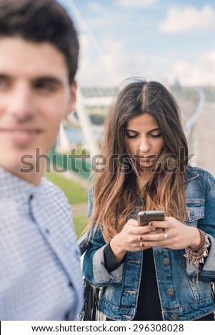 Woman distracted looking at her smart phone. The woman is not aware of her boyfriend.