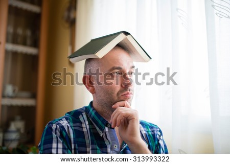 Adult man with a book on his head. He is thoughtfully