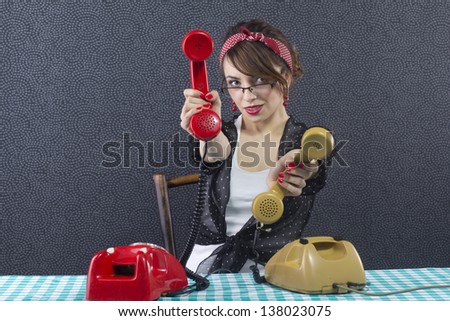 Sexy pin up secretary sitting at a desk, smiles and shows yellow and red phone