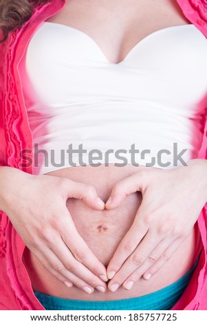 Pregnant woman making heart shape with hands over her stomach. Isolated over white background