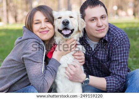 Smiling young man and woman hugging a Labrador retriever dog out in the park