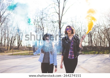 Two young girlfriends in sunglasses having fun with smoke bombs
