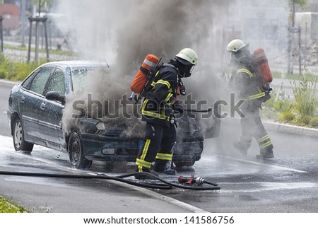 Burning motor vehicle been put out by firemen in protective clothing