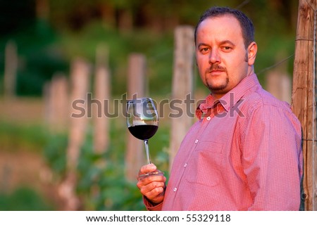 Young man is tasting red wine in the vineyard at sunset