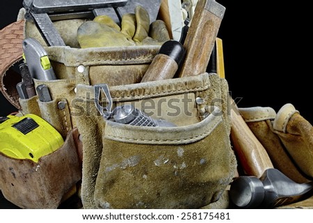 Rugged worn carpenters leather work bags and belt with construction tools and hammer isolated on black and selective focus on plumb and rule