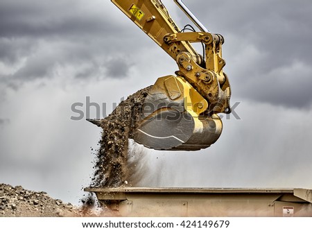 Construction industry heavy equipment excavator moving gravel at jobsite quarry with stormy skies