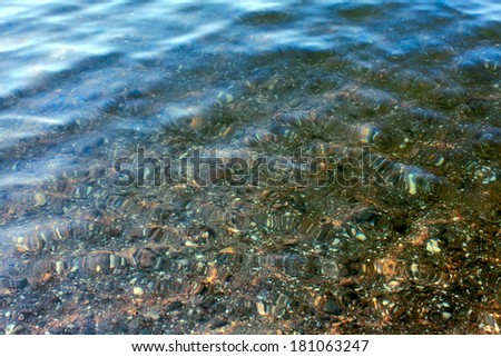 Seabed with pebble under water with solar patches of light. top view