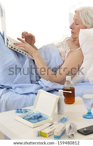 senior woman sick in bed with computer  with full of medicine foreground