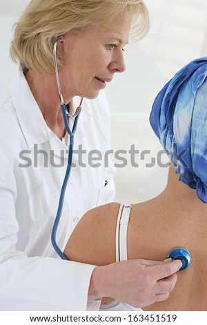 Doctor examining  cancer patient in a head scarf  with stethoscope