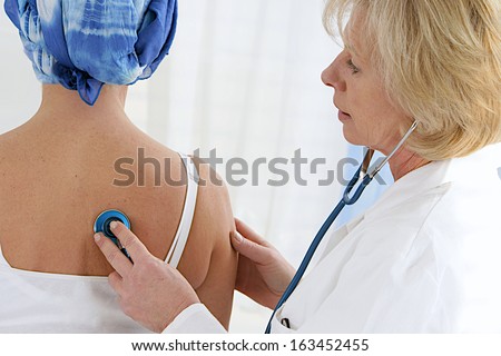 Doctor examining  cancer patient in a head scarf  with stethoscope