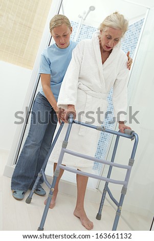 Elderly help keeping an elderly woman secure as she ambulates from  with his walker. On a white background.