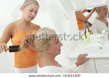 Young woman doing an hairbrush to old woman in front of the mirror
