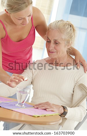Home-care nurse helping elderly lady to take her painkiller