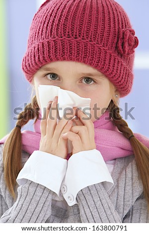 Sick little girl with an handkerchief and a pink hat blowing her nose