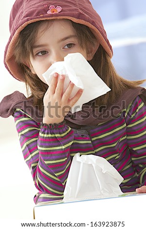 Sick little girl blows her nose, holding a tissue box