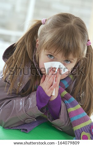 Sick little girl blows her nose, with a tissue