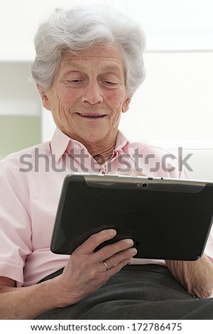 Smart Senior woman using a laptop at home sitting on the sofa   reading information on the screen with a smile