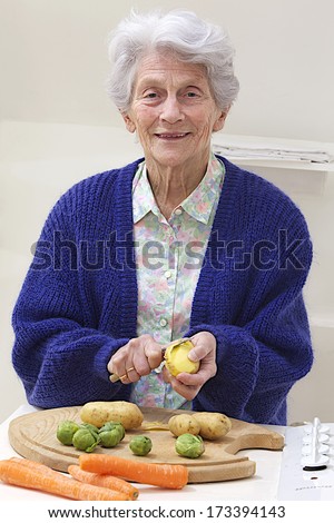 Senior woman peeling and slicing raw vegetables on a cutting board. she is looking at the camera