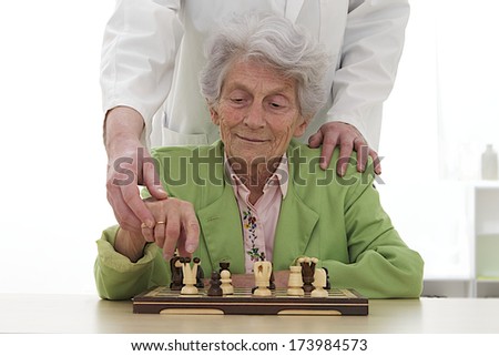senior woman helped to play chess with care giver-Re-education center