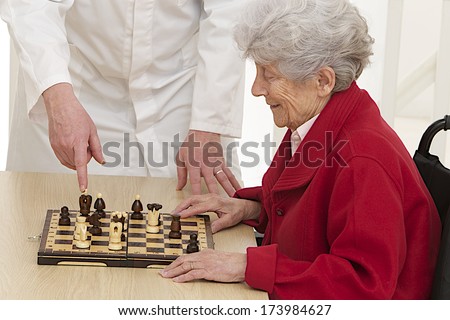 disabled senior woman playing chess with care giver-Re-education center