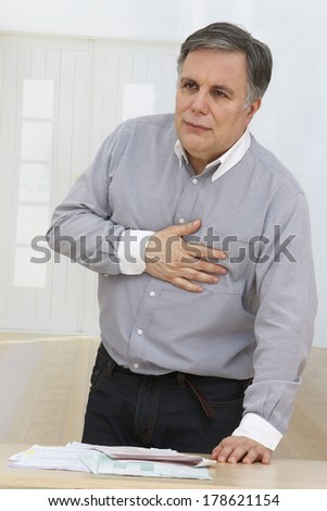 A mature man having a heart pain in his living room, after racing financial paper