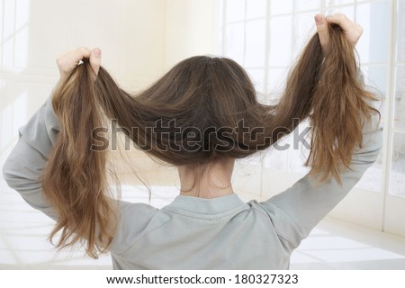Brunette lady holding long hairs, view from back side isolated on white